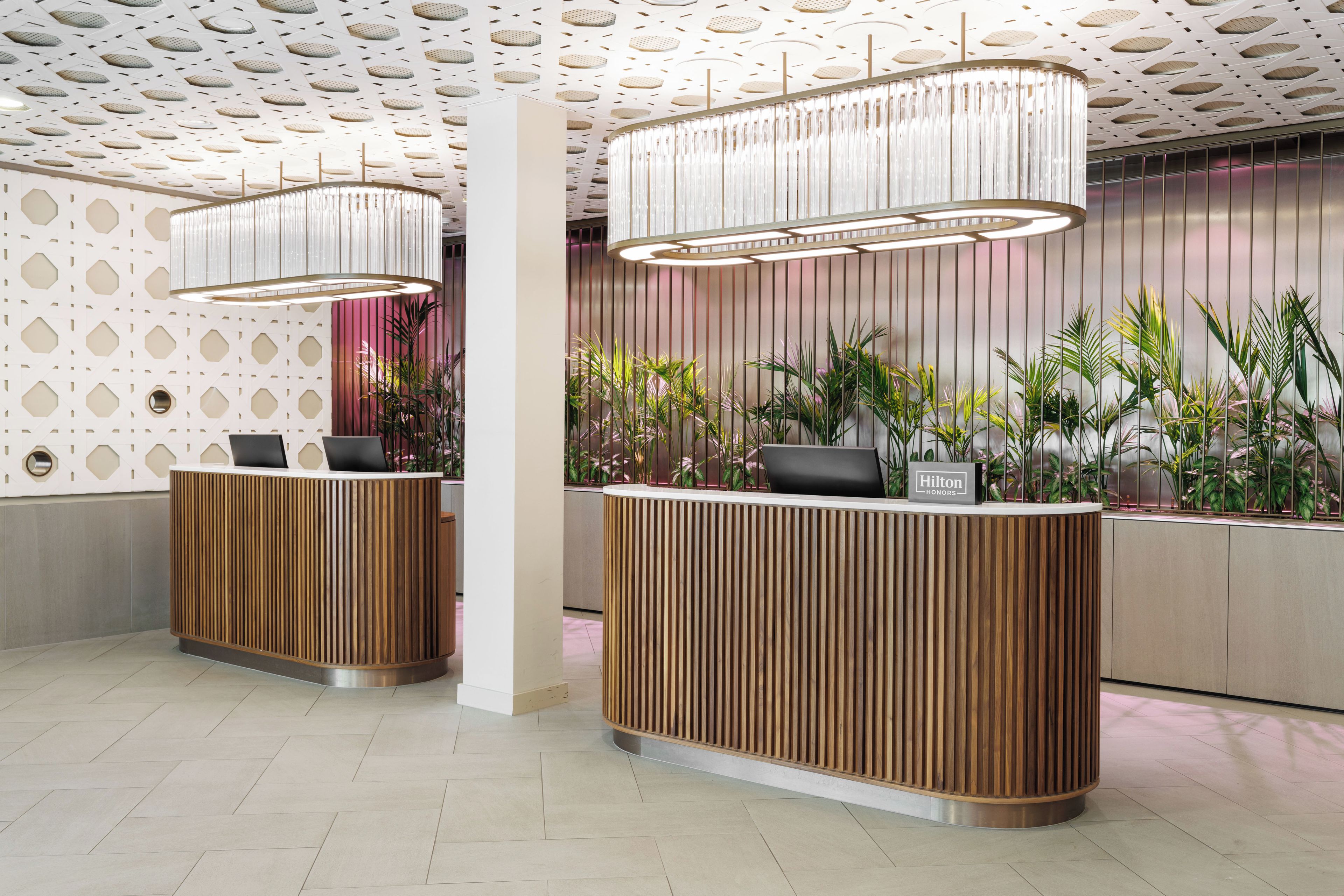 A hotel reception area with a modern design, featuring a wooden reception desk, a large chandelier, and a patterned ceiling.