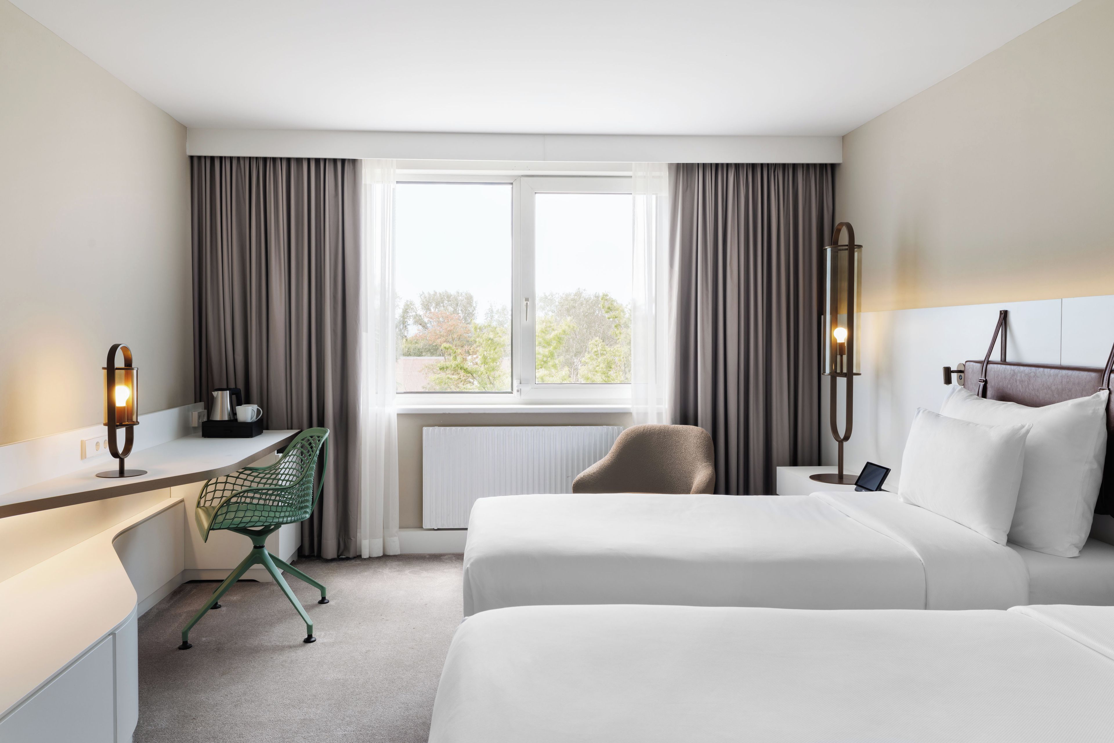Ein Hotelzimmer mit Bett, Schreibtisch, Stuhl und Blick auf Bäume durch das Fenster.
