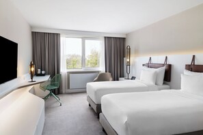 A hotel room with two beds, a desk with a chair, a TV, and a window with curtains. - DoubleTree by Hilton Vienna Bosei (Vienna)