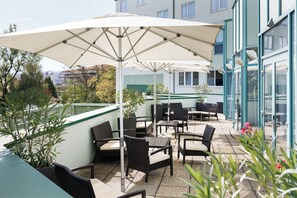 An outdoor seating area with tables and chairs, a large umbrella, and potted plants. - DoubleTree by Hilton Vienna Bosei (Vienna)