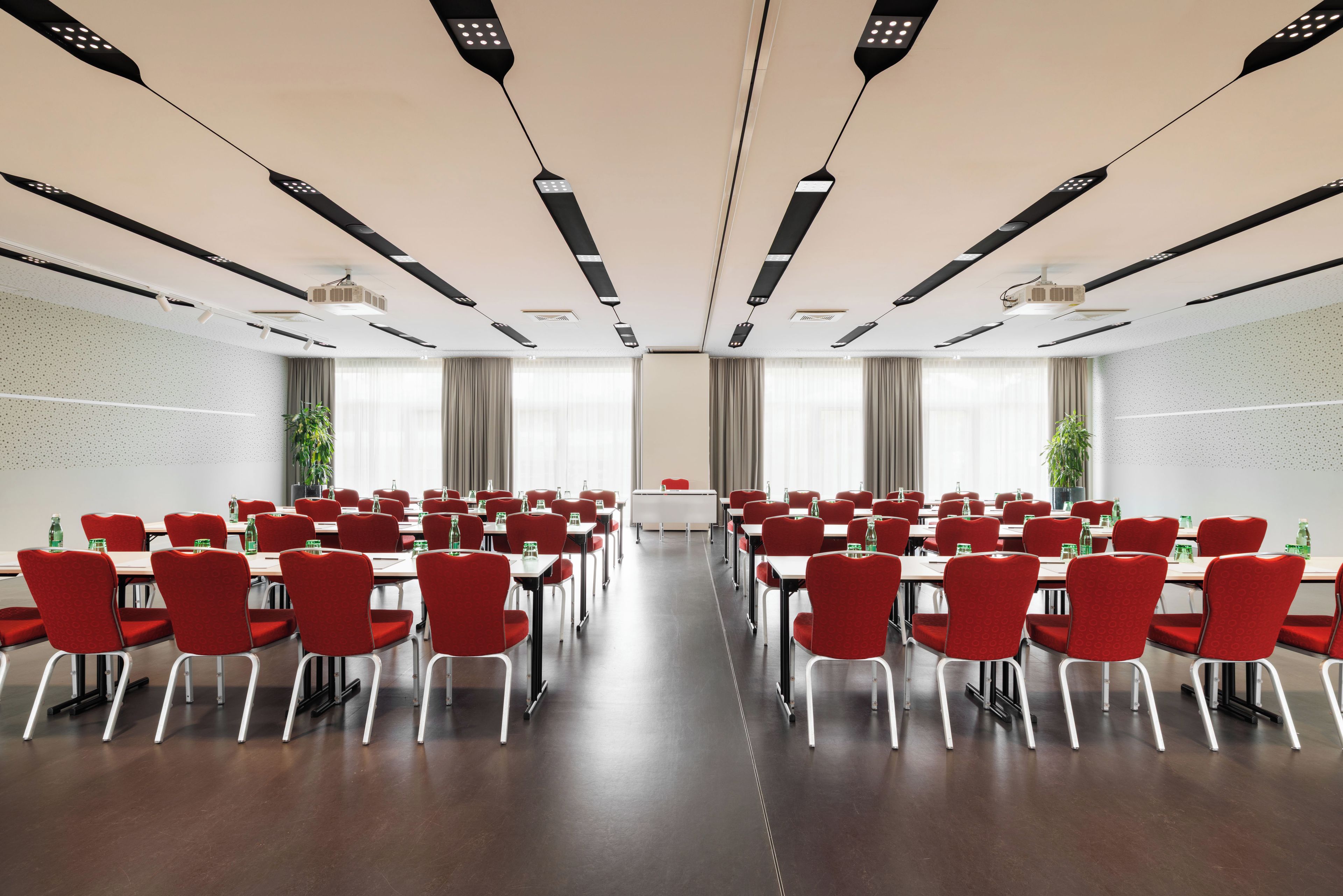 A conference room with rows of tables and chairs, large windows, and ceiling-mounted projectors.
