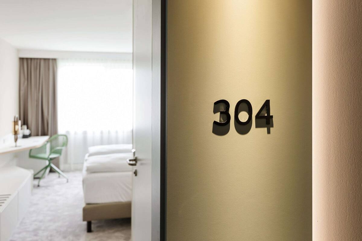 A hotel room with a bed, a desk, and a chair. The room has a number sign '304' on the wall.