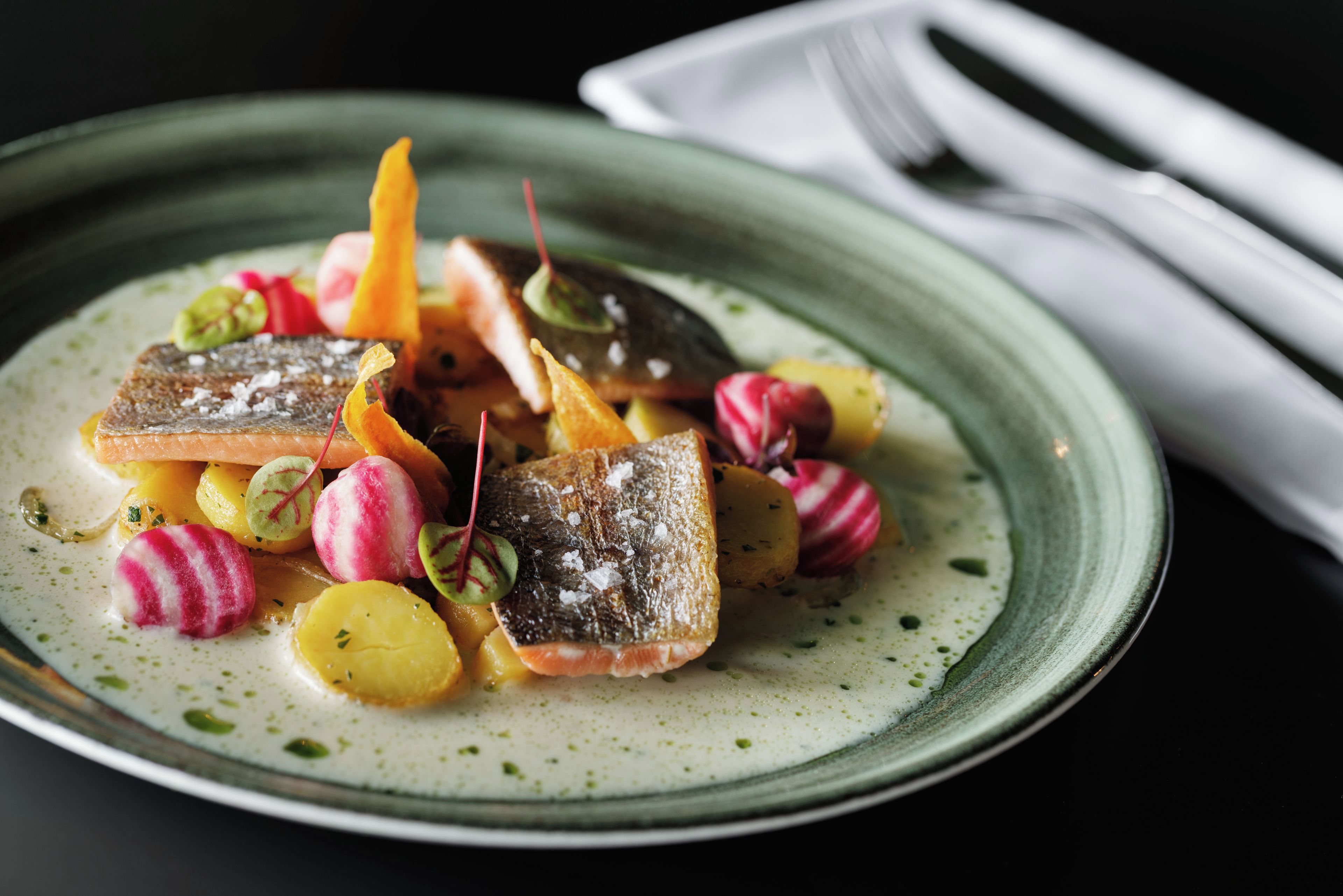 A plate of food with various vegetables and a fish, served on a ceramic plate.