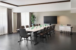 Un salón de conferencias con una larga mesa, sillas, un televisor de pantalla plana grande y una planta en maceta.