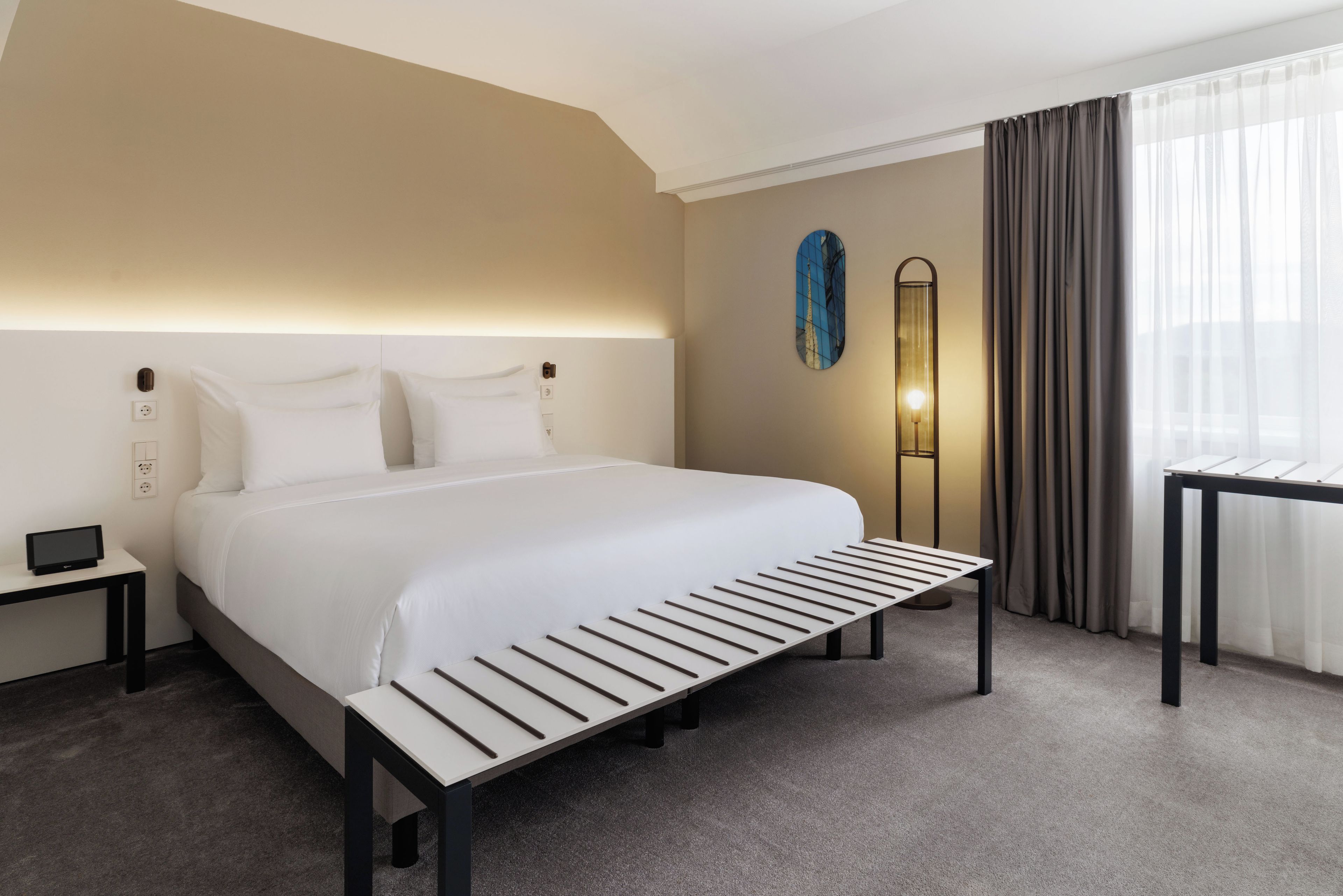 A hotel room with a large bed, bedside tables, a floor lamp, and a view of the Eiffel Tower through a window.