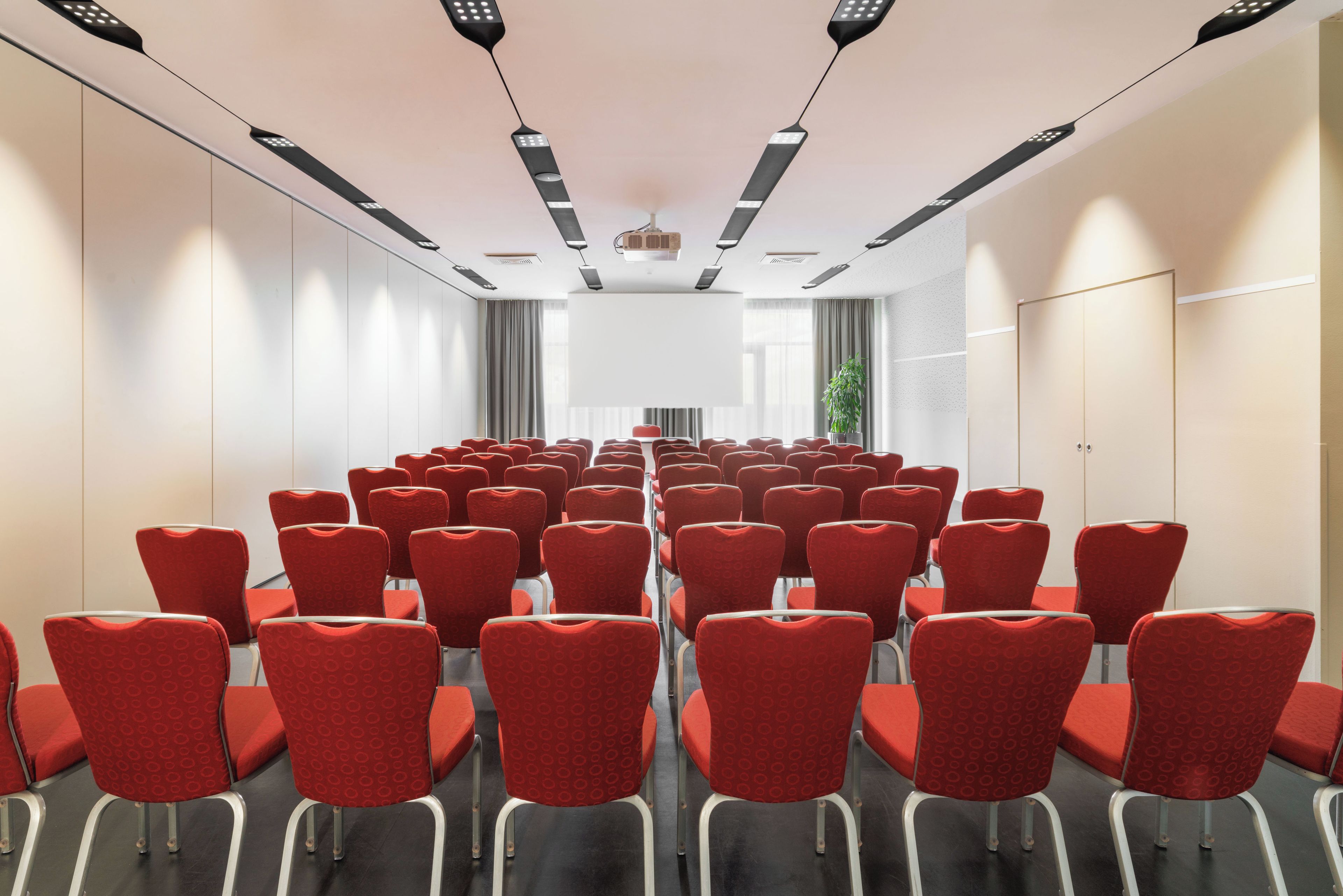 A conference room with rows of red chairs, a projector screen, and a whiteboard.