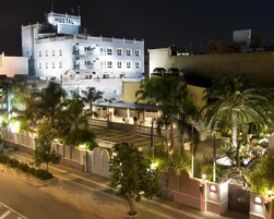Un hotel con un llamativo letrero que dice 'HOSTAL', rodeado de palmeras y senderos bien iluminados.