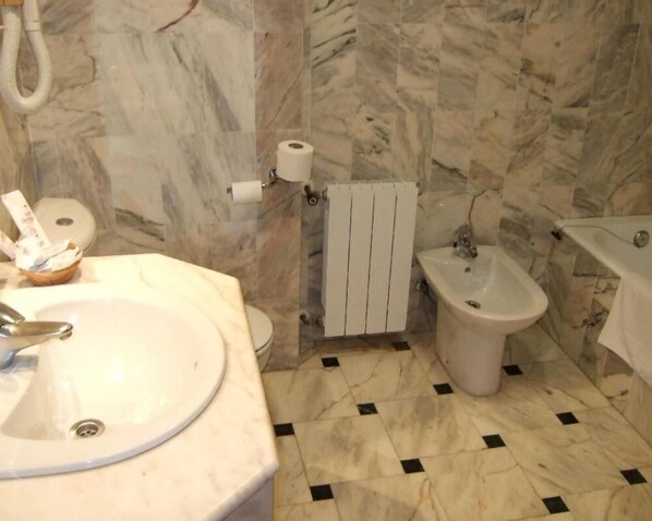 Ein Badezimmer mit Waschbecken, Bidet, Toilette, Marmorwänden und Fliesenboden.