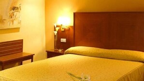 A hotel room with a large bed, a wooden headboard, a nightstand with a lamp, a small table, and a painting on the wall. - Casa Quiquet (Beniparrell)