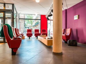 Un área de espera moderna con sillas rojas, una mesa de recepción y vista a la calle.