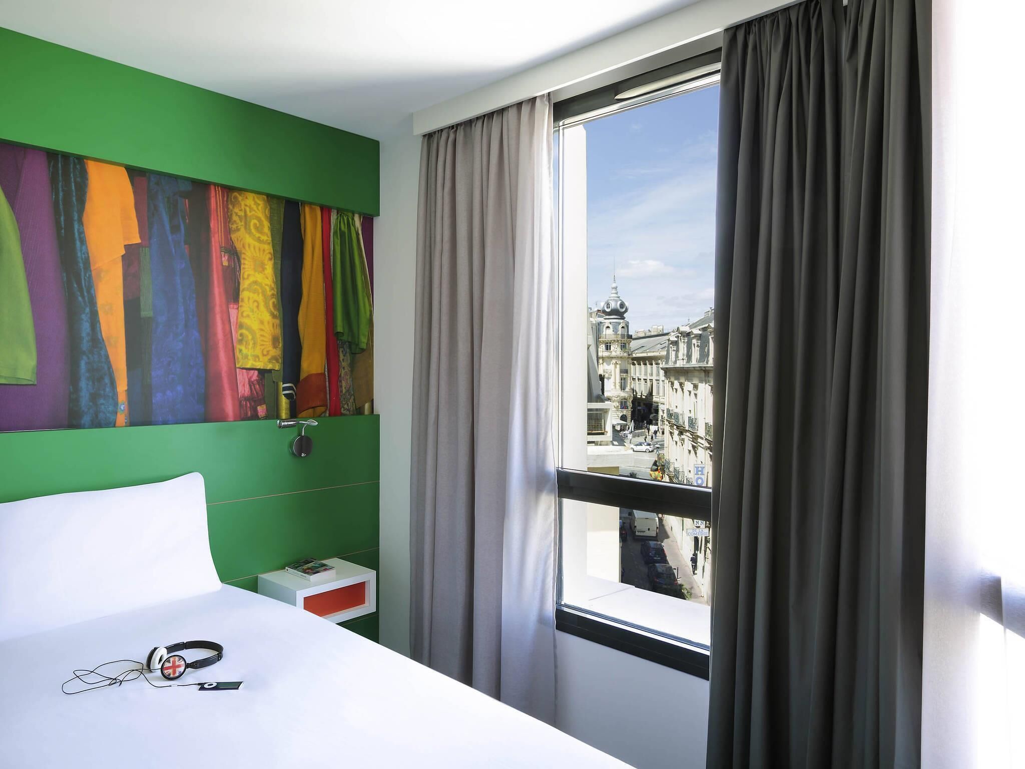 Ein Hotelzimmer mit großem Fenster, einem Bett, einer grünen Wand und einem farbenfrohen abstrakten Gemälde.