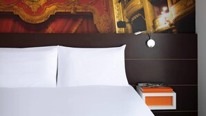 Une chambre d’hôtel avec un grand lit, une tête de lit ornée d’une horloge et un mur décoré de motifs complexes.