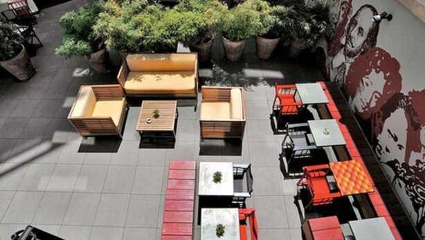 Un espace extérieur aménagé avec plusieurs tables et chaises, entouré de plantes en pot et orné d’une fresque murale.