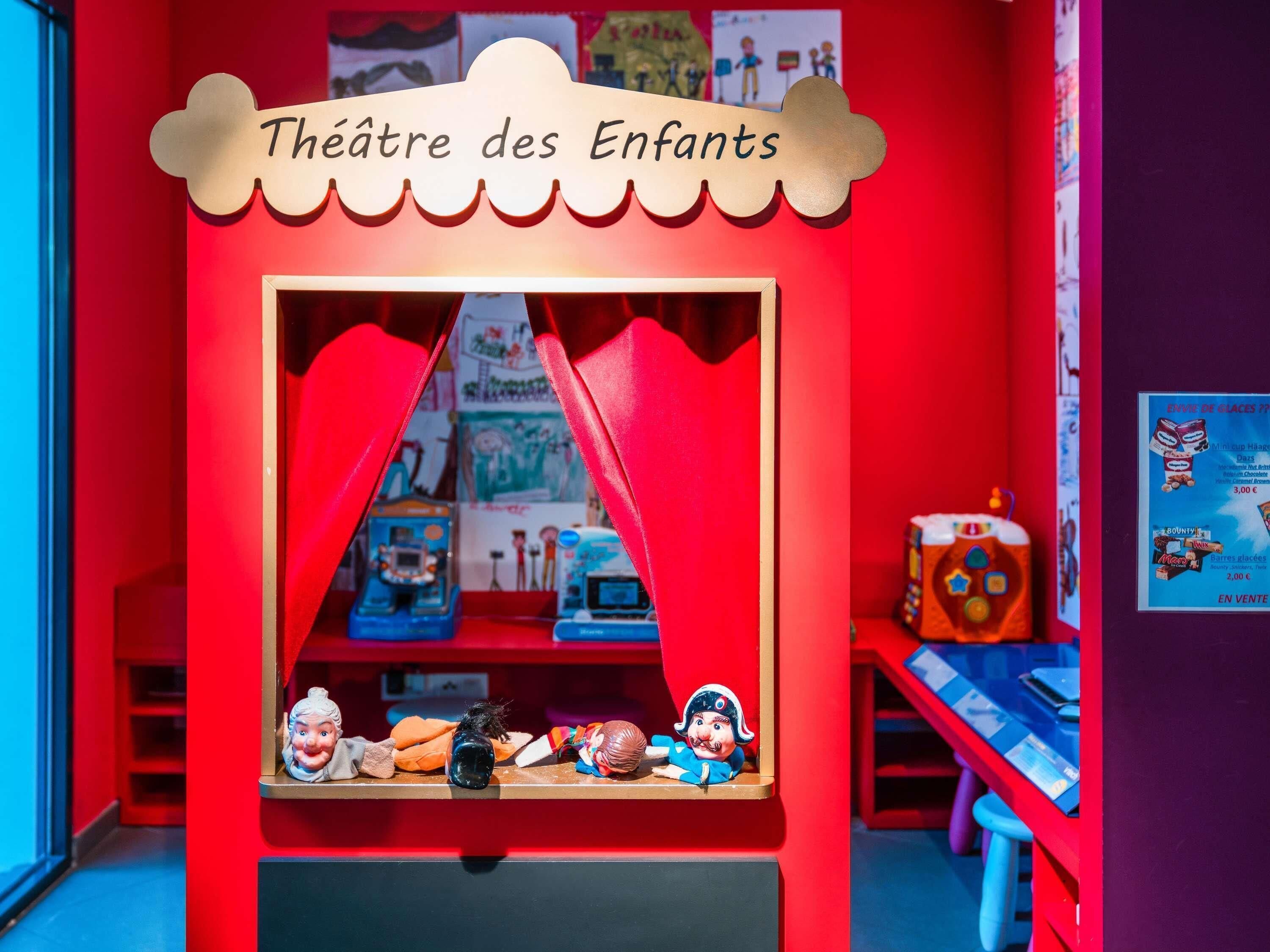 Um teatro infantil com interior vermelho, apresentando uma área de palco com um cenário e diversos brinquedos e bonecos expostos em prateleiras.