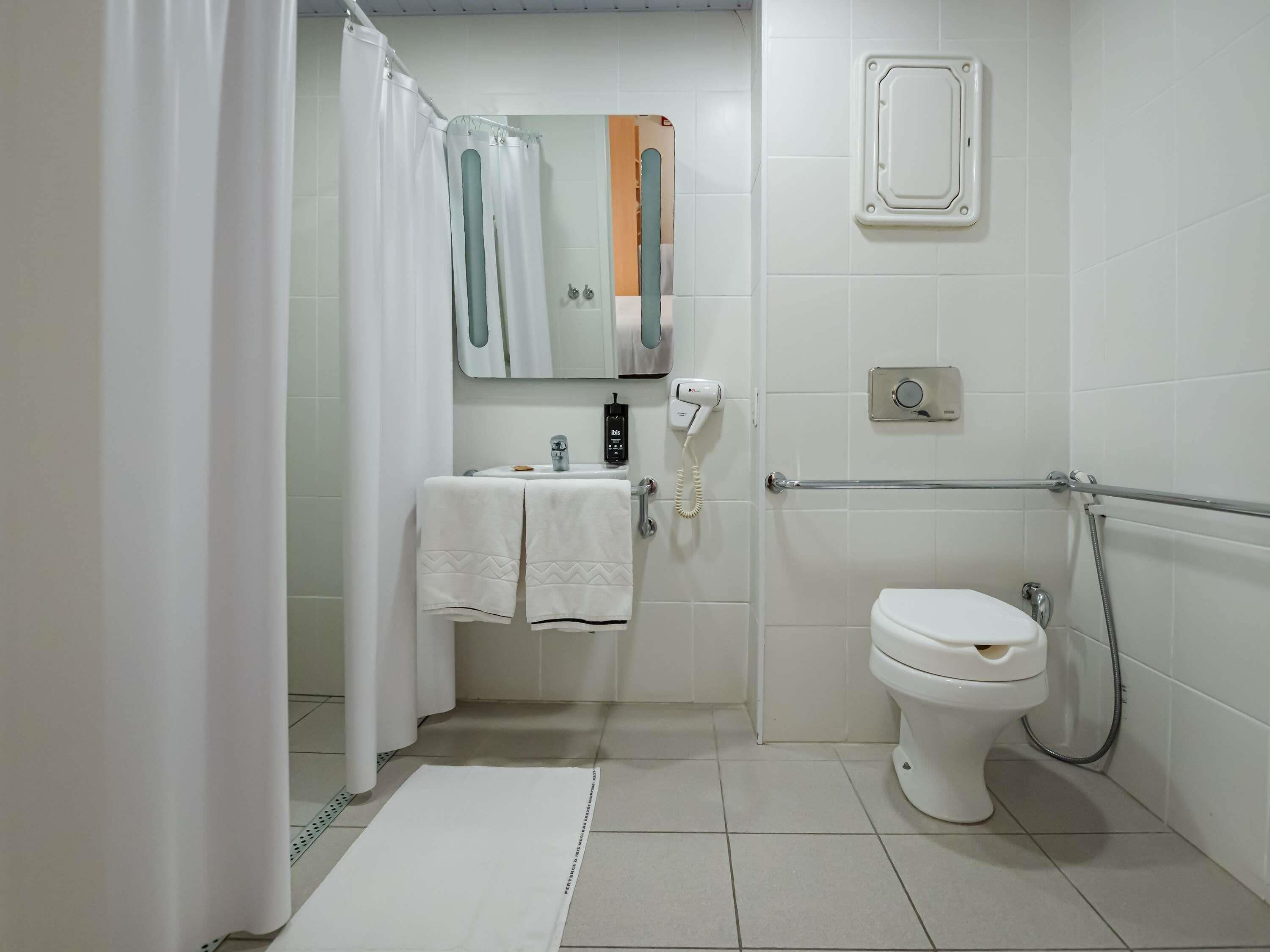A bathroom with a toilet, a sink with a towel, a shower curtain, a mirror, and a handheld showerhead.
