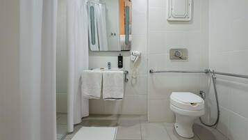 A bathroom with a toilet, a sink with a towel, a shower curtain, a mirror, and a handheld showerhead.