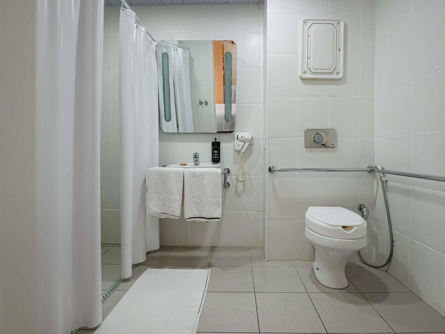 A bathroom with a toilet, a sink with a towel, a shower curtain, a mirror, and a handheld showerhead.