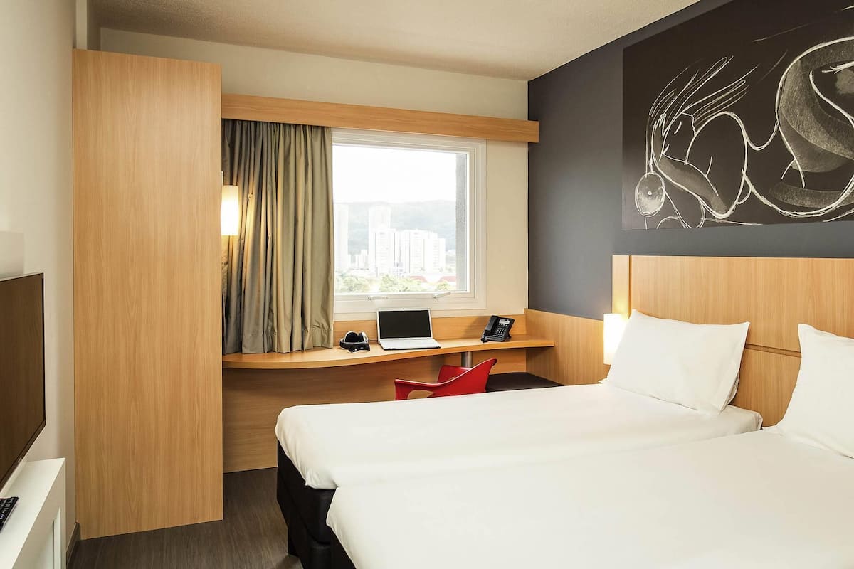 A hotel room with a bed, a desk with a laptop, a telephone, and a chair.
