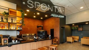 Un bar à pizzas avec une enseigne distinctive, un comptoir en bois, des tabourets de bar et des étagères remplies de bouteilles.