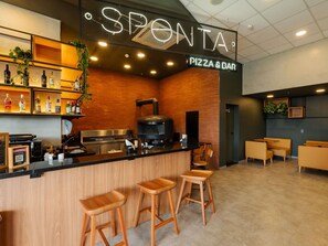 A pizza bar with a branded sign, a wood-paneled counter, bar stools, and shelves with bottles.