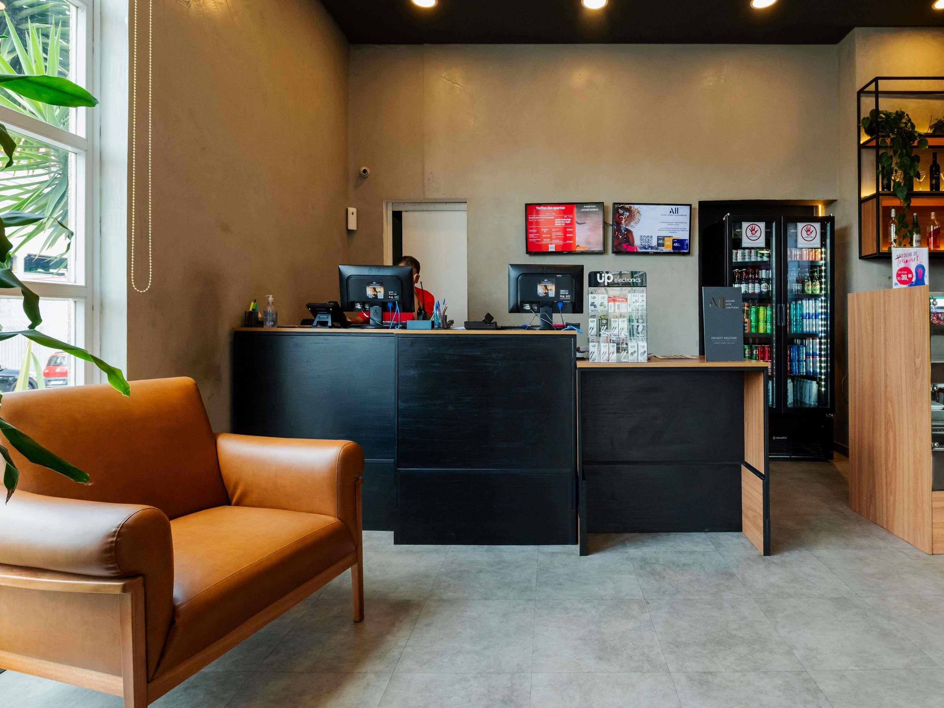 Zona de recepción con mostrador, computadora y refrigerador lleno de bebidas.