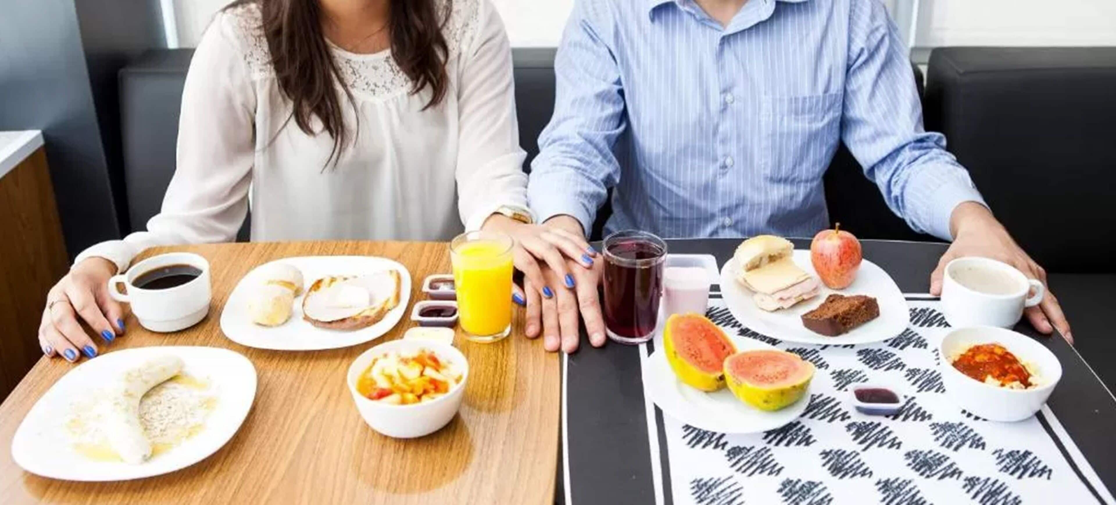 Un desayuno con dos personas sentadas en una mesa, con diferentes alimentos y bebidas.