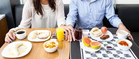 Un desayuno con dos personas sentadas en una mesa, con diferentes alimentos y bebidas.