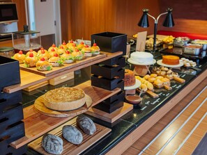 Monipuolinen buffet, jossa on tarjolla erilaisia ruokia, kuten voileipiä, kakkuja ja leivonnaisia.