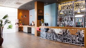 Un espace d’accueil moderne avec un comptoir en bois, un coin salon avec des fauteuils à motifs et un mur orné d’œuvres d’art abstraites.