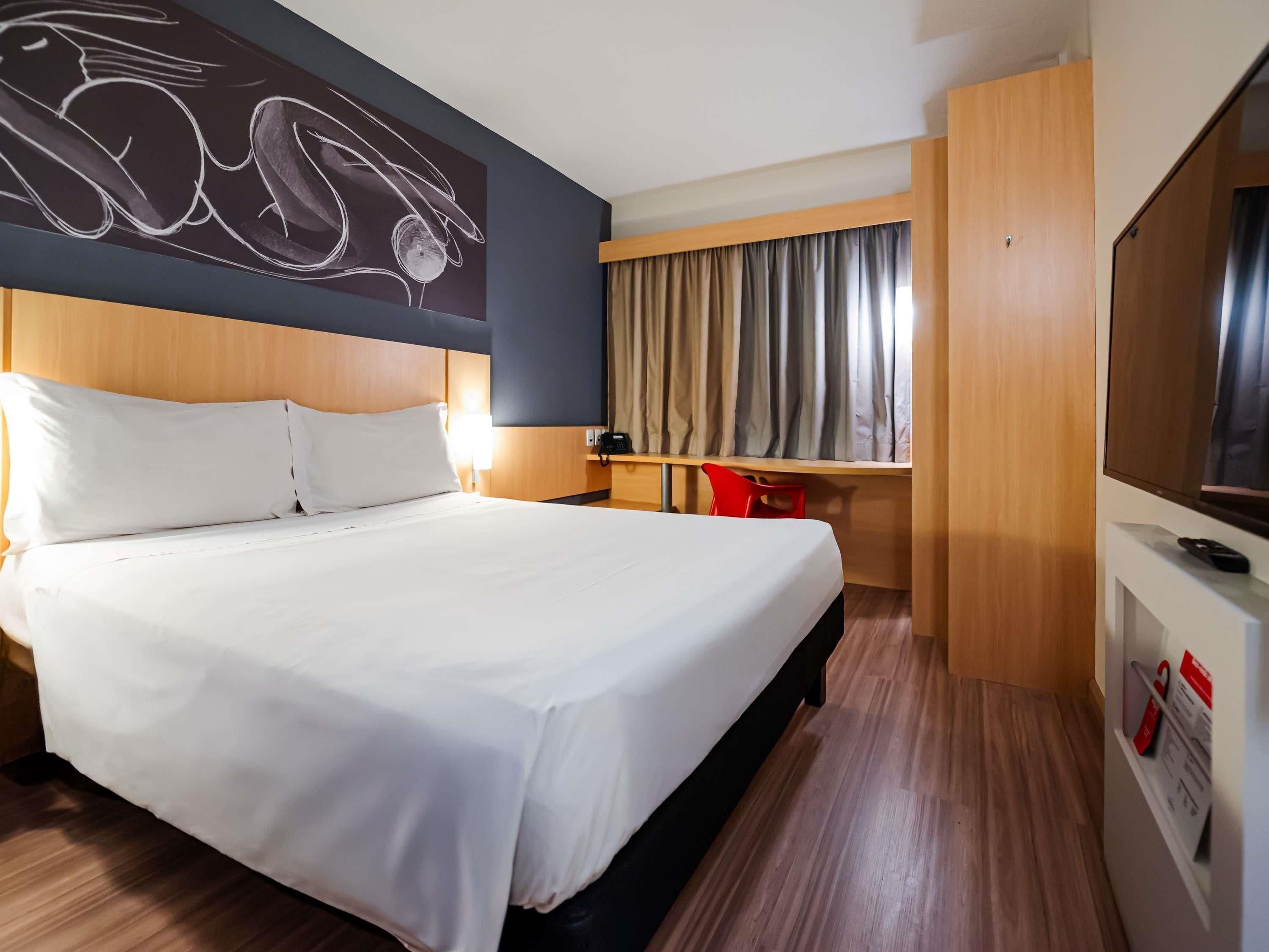 Habitación de hotel con una cama grande, un escritorio, una silla, un televisor y una obra de arte en la pared.