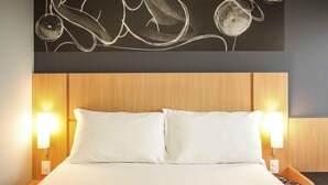 Une chambre d’hôtel avec un lit, deux lampes de chevet, une tête de lit en bois et une œuvre d’art murale.