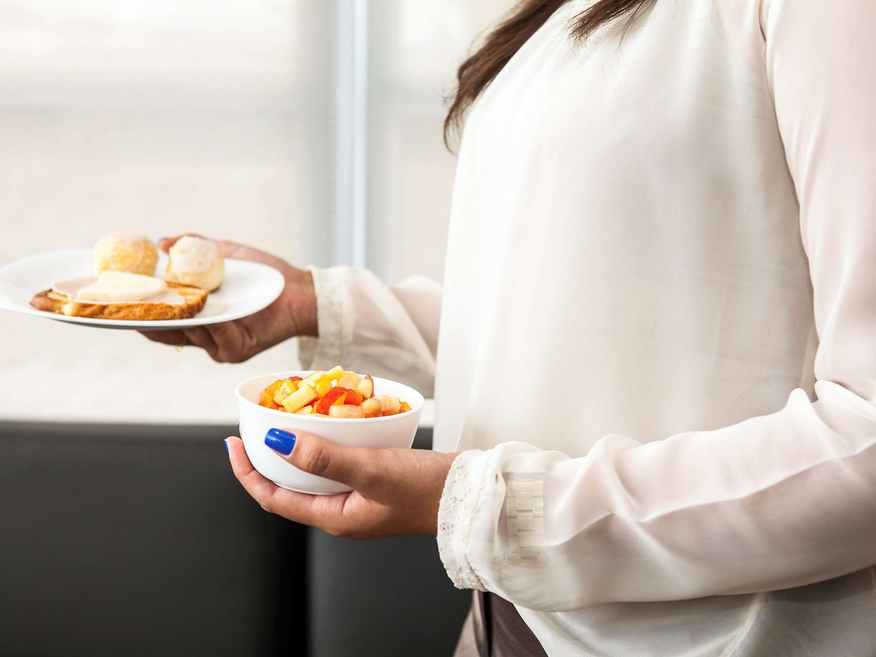 Eine Person hält einen Teller mit Brot und eine Schüssel mit Obst.