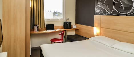Una habitación de hotel con una cama, un escritorio con una laptop, una silla roja, una ventana con cortinas y una pared con una obra de arte abstracta de gran tamaño.