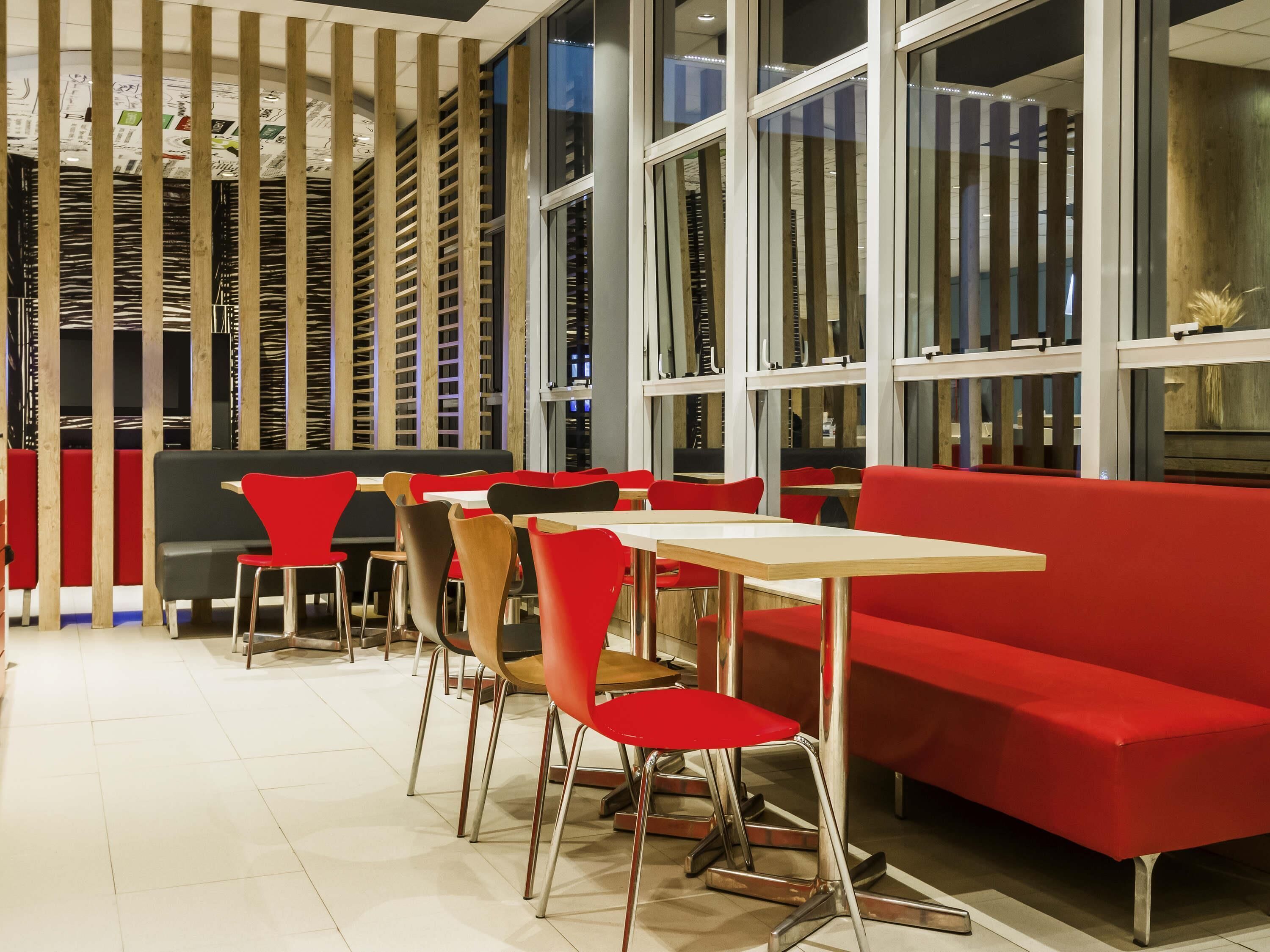 Un comedor moderno con mobiliario rojo y negro, ventanas amplias y una pared de listones de madera.