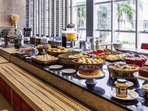 A buffet with various food items, a coffee station, and a view of palm trees through large windows.