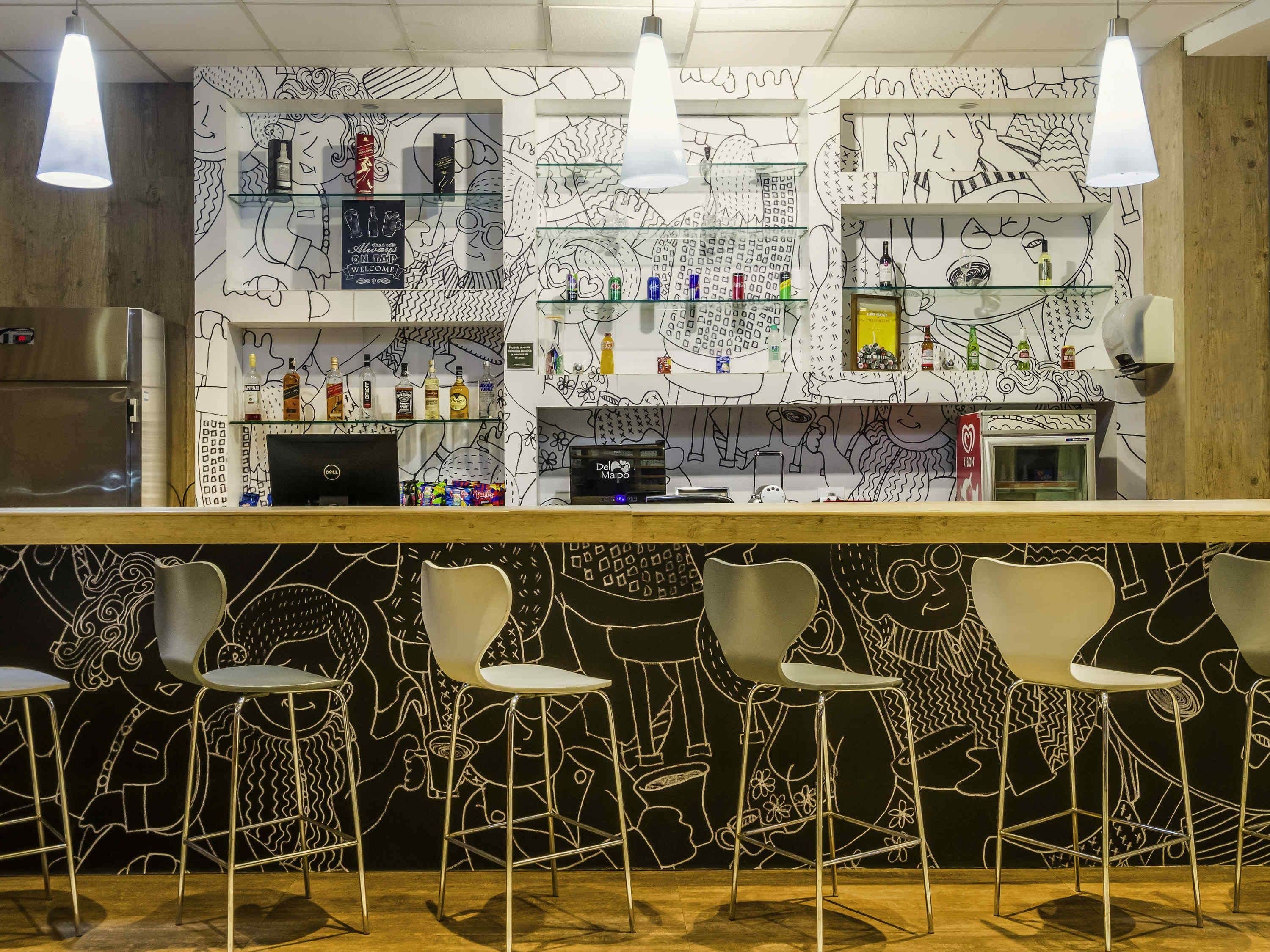 Zona de bar con mostrador, taburetes y estantes con botellas.