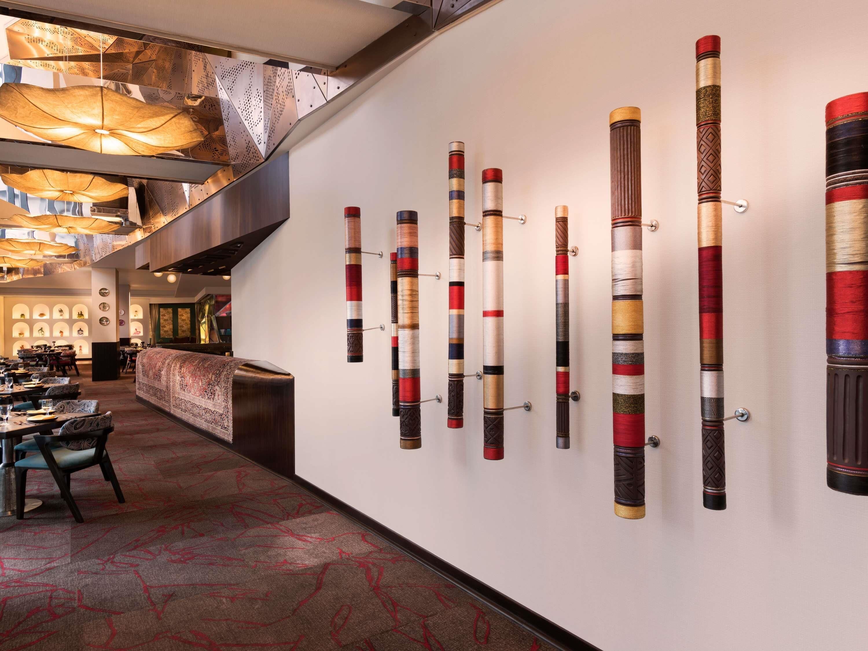 A modern hotel lobby with a long reception desk, a staircase, and a wall displaying various wooden artifacts.