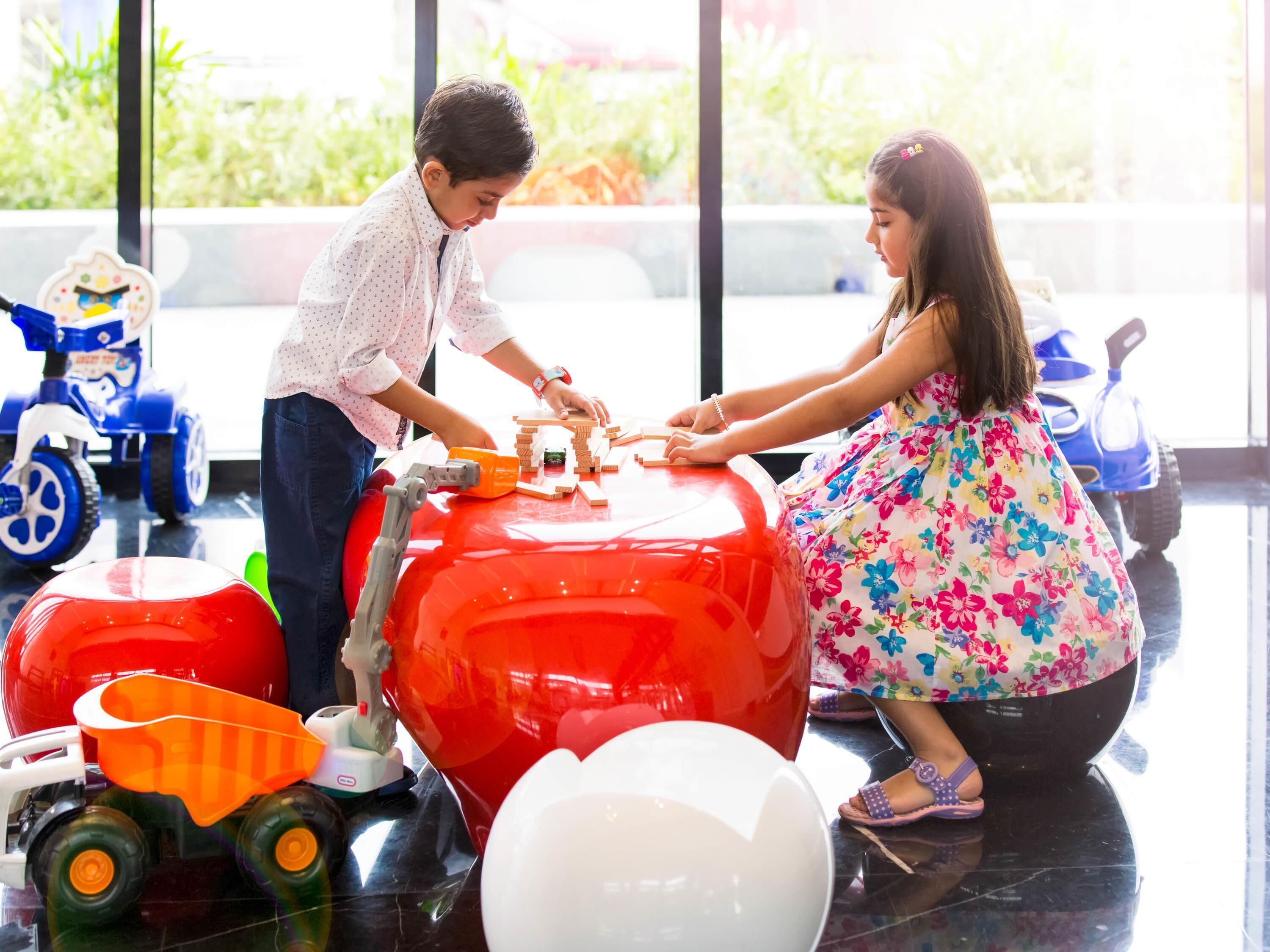 A child and an adult playing with toys and a large red balloon on a shiny floor.