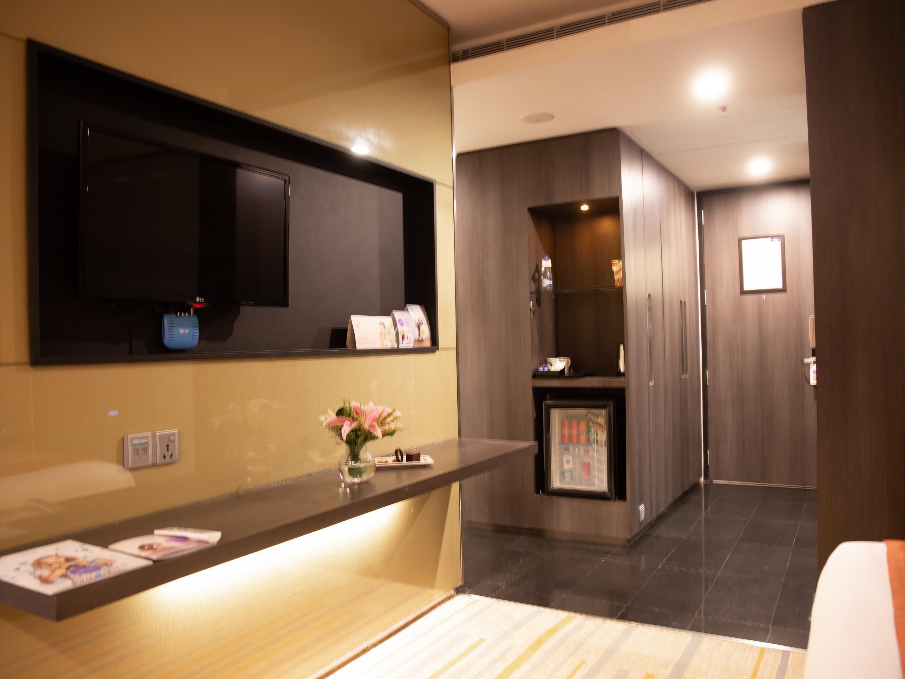 A hotel reception area with a reception desk, a small refrigerator, a mirror, and a wall-mounted television.