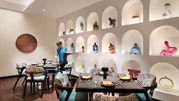 Un espace repas avec un serveur, un élément décoratif circulaire fixé au mur et une série d’étagères ornées de différents vases.