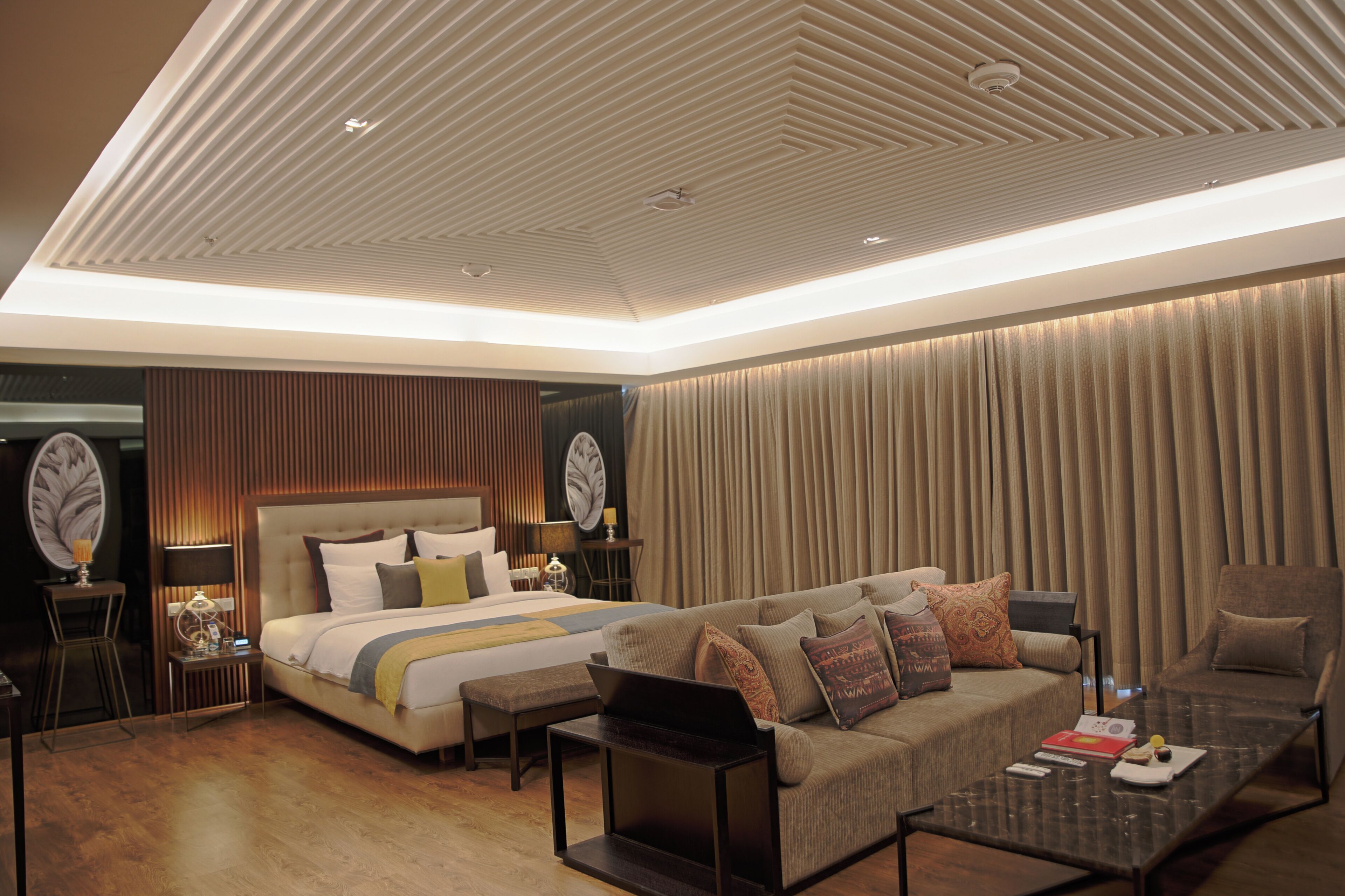 A modern hotel room with a large bed, a sofa, a coffee table, and a desk.