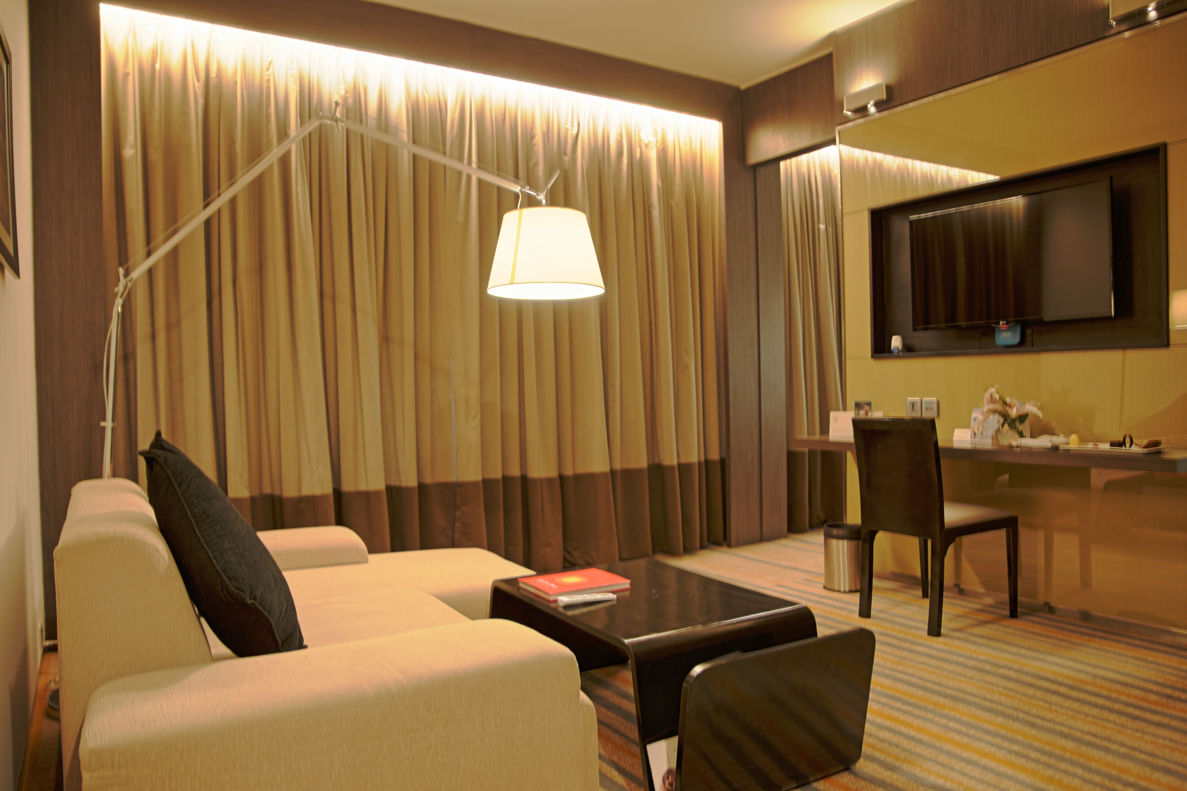 A hotel room with a sofa, a coffee table, a desk, and a television.