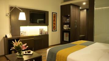 Une chambre d’hôtel équipée d’un lit, d’un bureau, d’une télévision, d’un mini-bar et d’une grande fenêtre.