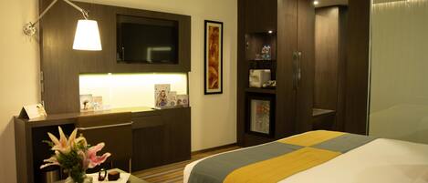 Una habitación de hotel con cama, escritorio, televisor, minibar y un amplio ventanal.
