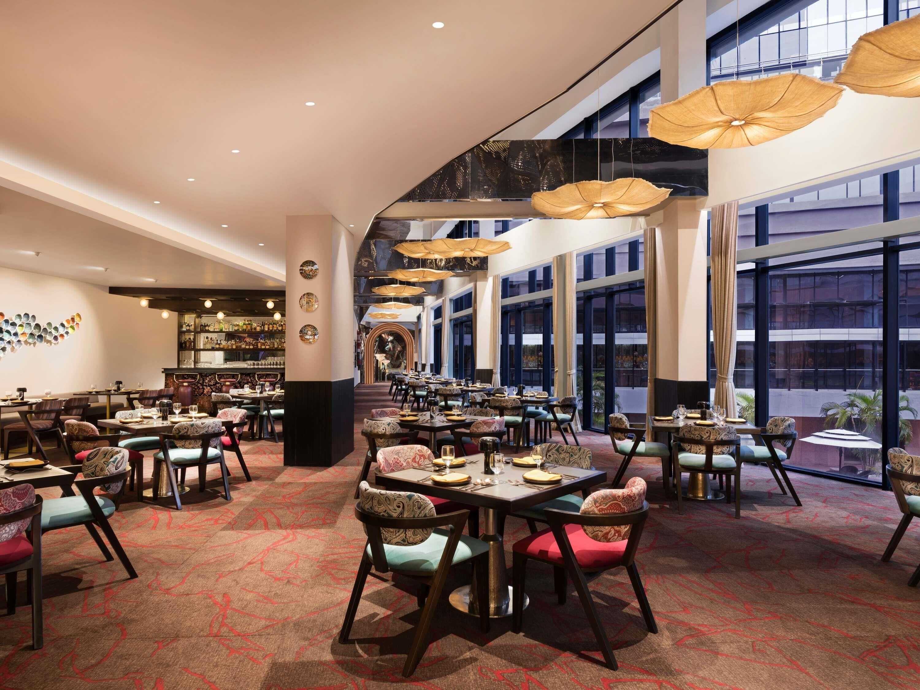 Un vaste espace dédié à la salle à manger, avec de nombreuses tables et chaises, de grandes fenêtres et des lampes suspendues.