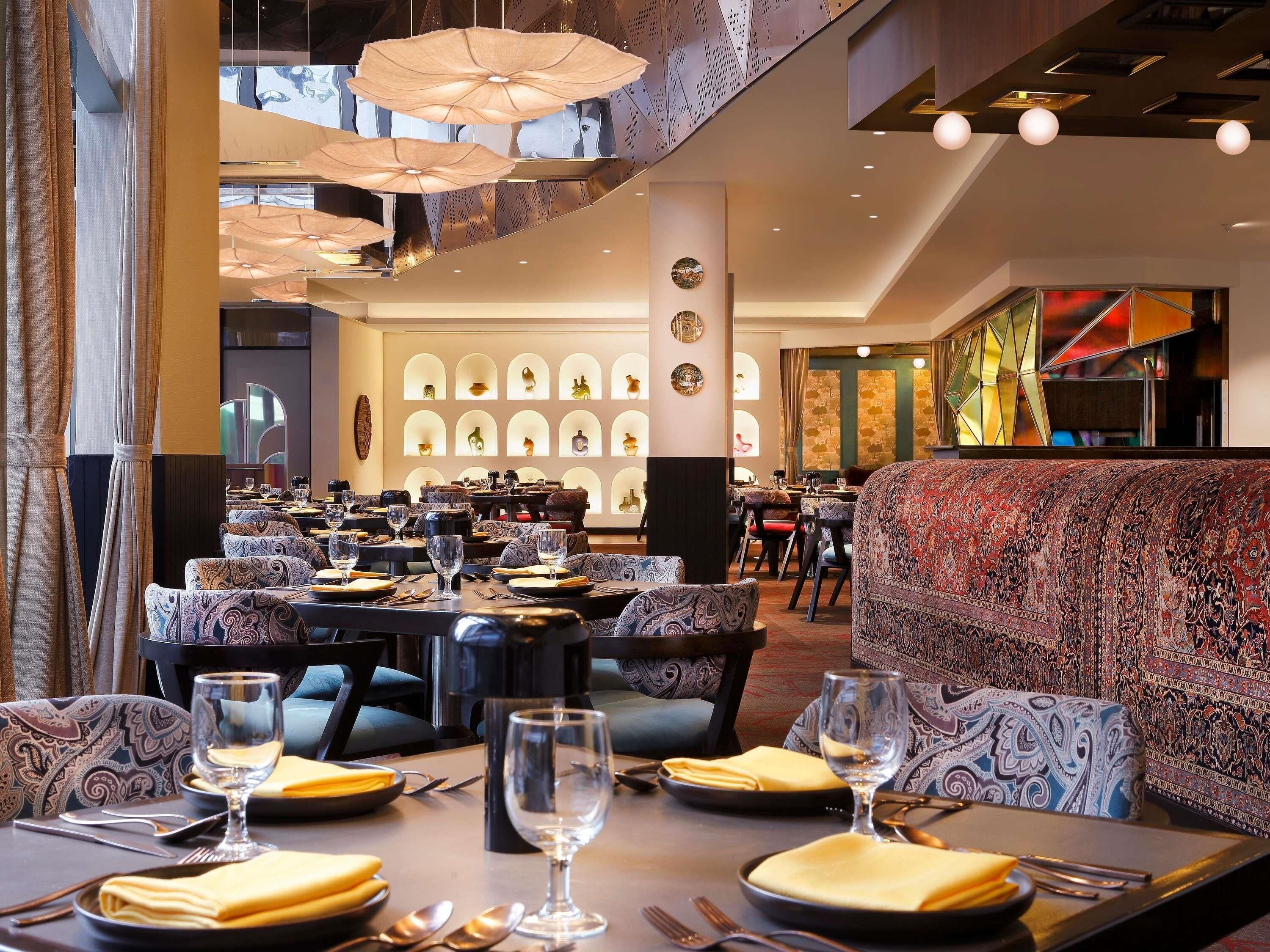A restaurant with multiple tables and chairs, a patterned sofa, and hanging lamps.