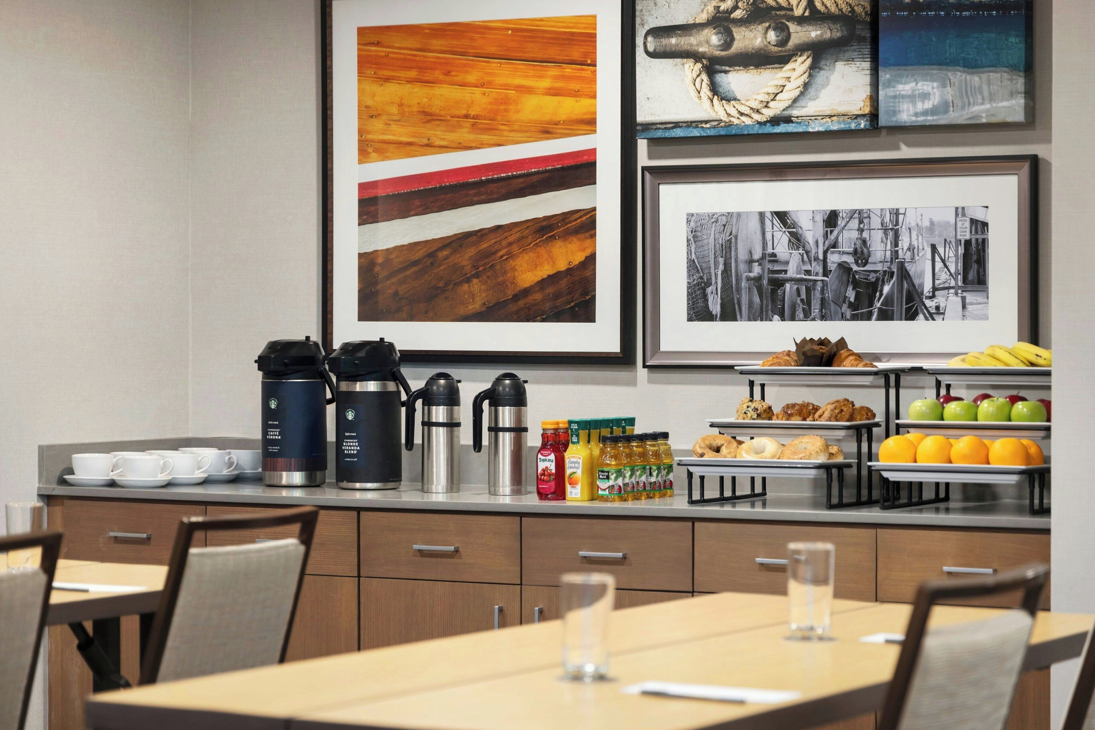 A modern kitchen with a coffee station, breakfast items, and framed artwork on the wall.