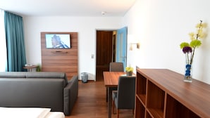 Una habitación de hotel moderna con sofá, mesa de comedor y televisor montado en la pared.
