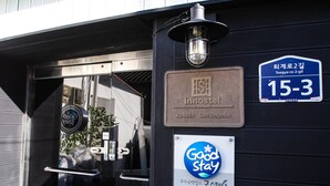 Ein Hotel Eingang mit einem Schild, das die Zimmernummer 15-3 anzeigt, einem Schild mit der Aufschrift 'Good Stay' und einem 'Innostel'-Schild.