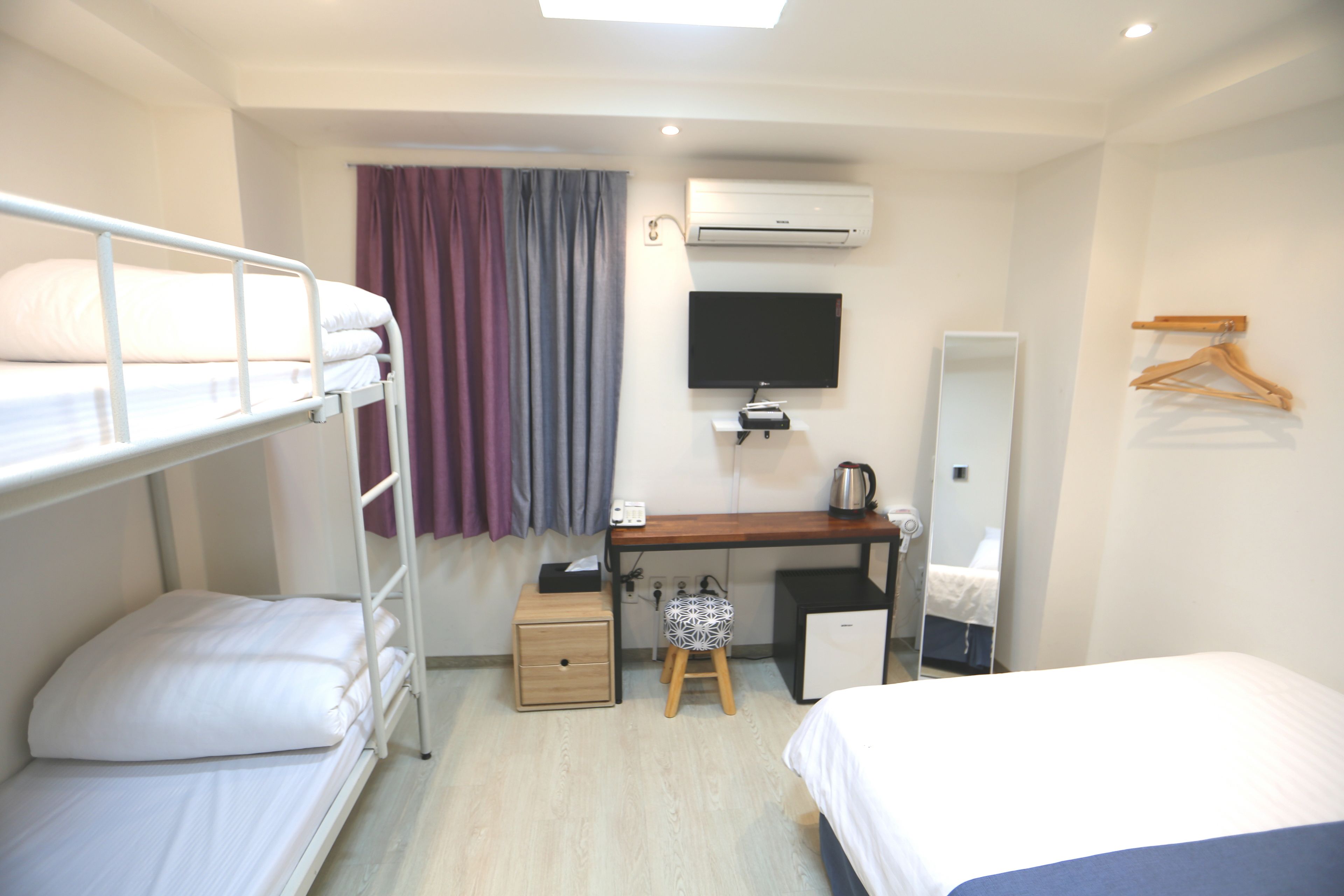 A hotel room with bunk beds, a desk with a computer, a small cabinet, a mirror, and a TV.